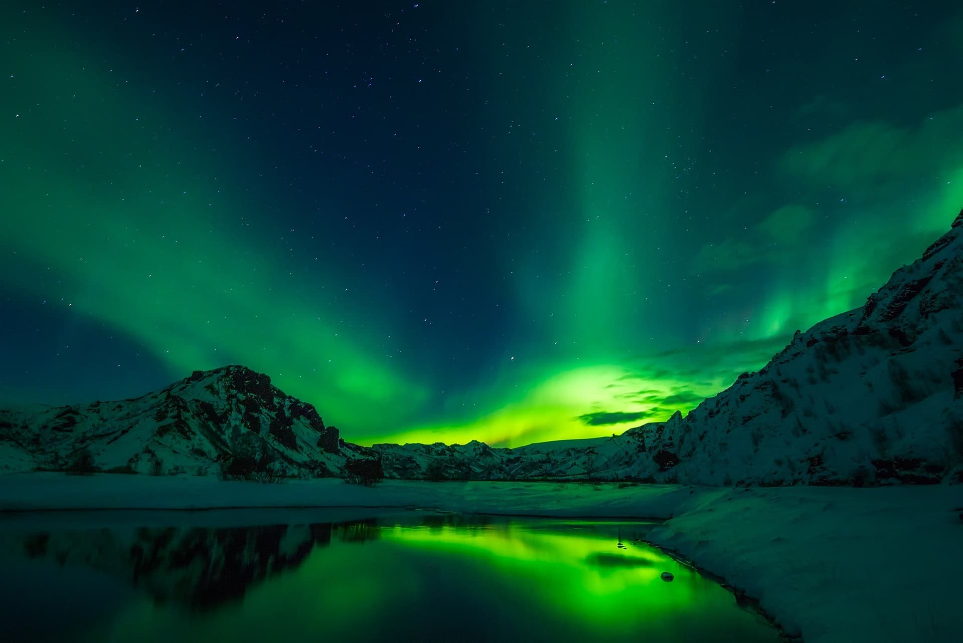 Northern lights reflected over a snow-covered mountain valley.